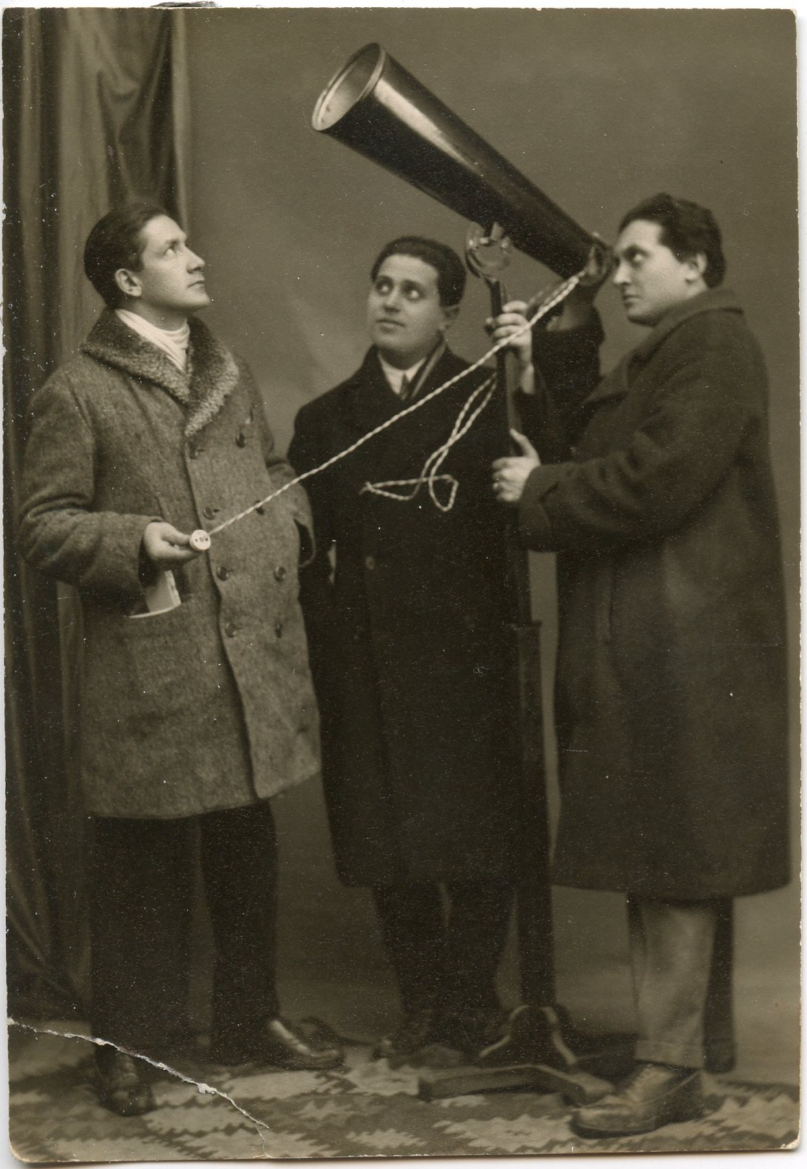 Ancienne photo de trois personnes, l’une regardant à travers un cône tandis qu’une autre tient une ficelle attachée.