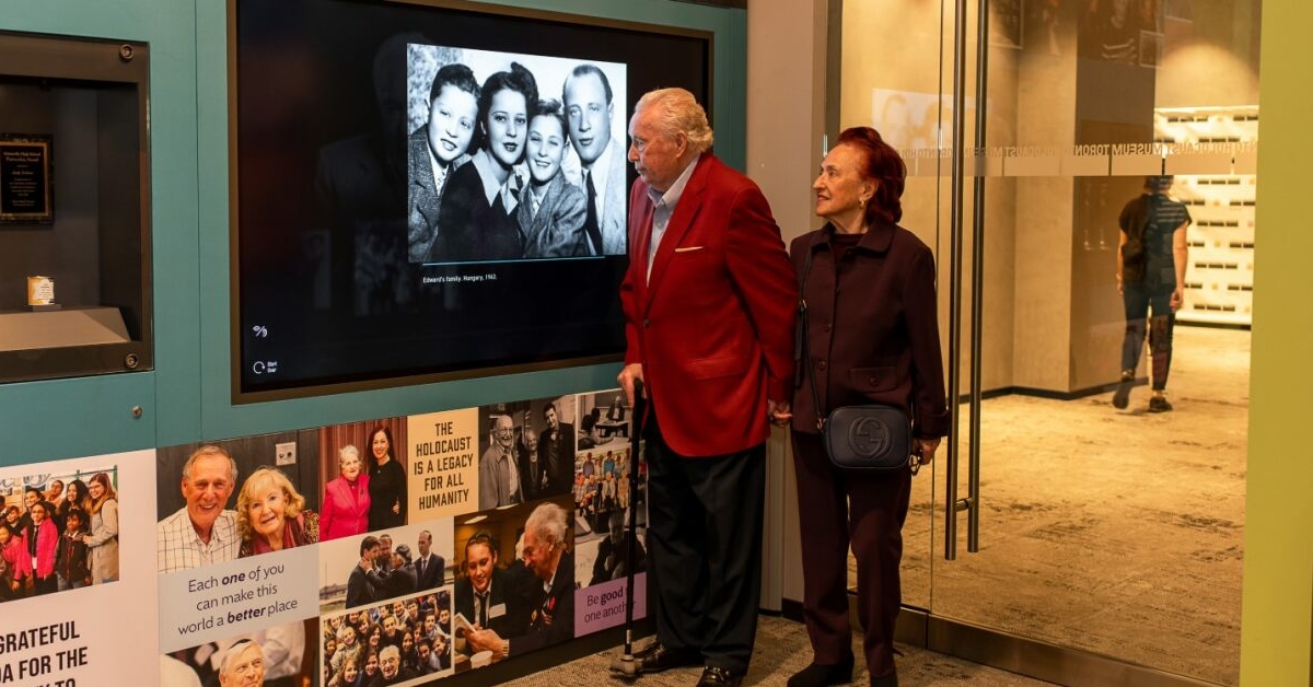 Deux personnes âgées se tiennent devant l'écran d'un musée où est projetée une photo en noir et blanc.