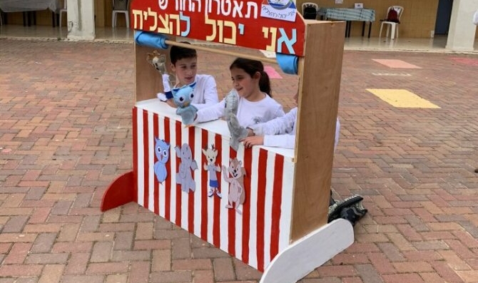 Trois jeunes enfants jouant avec des marionnettes derrière un théâtre de marionnettes à rayures rouges et blanches.