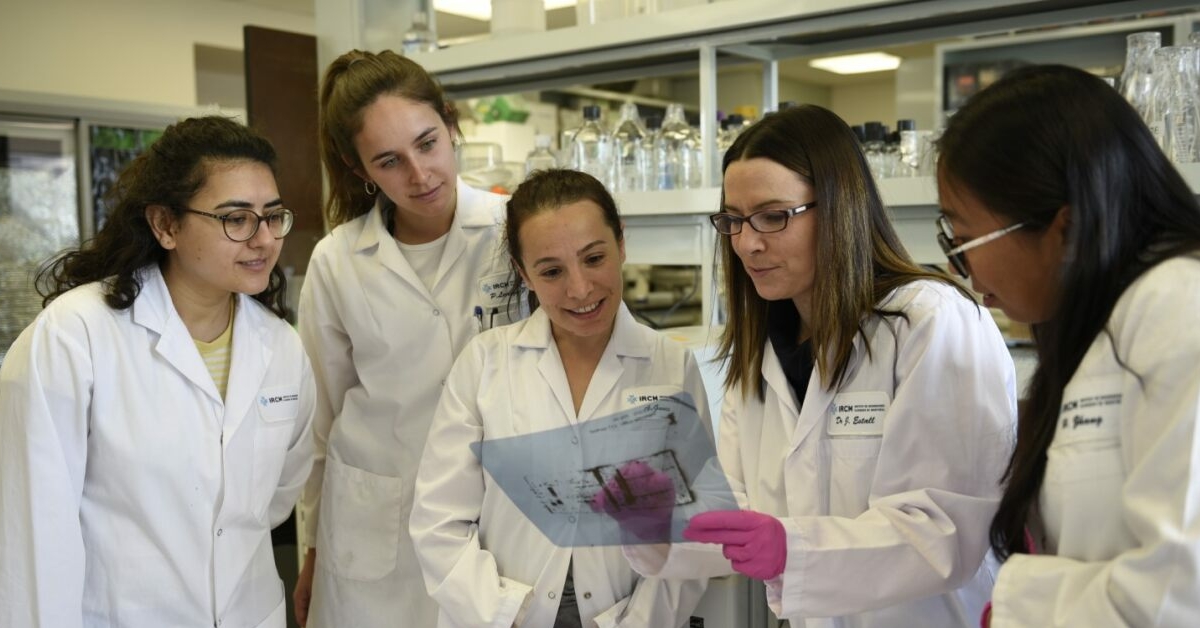 Cinq scientifiques dans un laboratoire. L'une d'eux porte des gants roses et brandit une feuille de papier sous le regard des quatre autres.