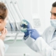 Un dentiste portant un masque médical tient des fausses dents pendant qu'il s'occupe d'un patient.