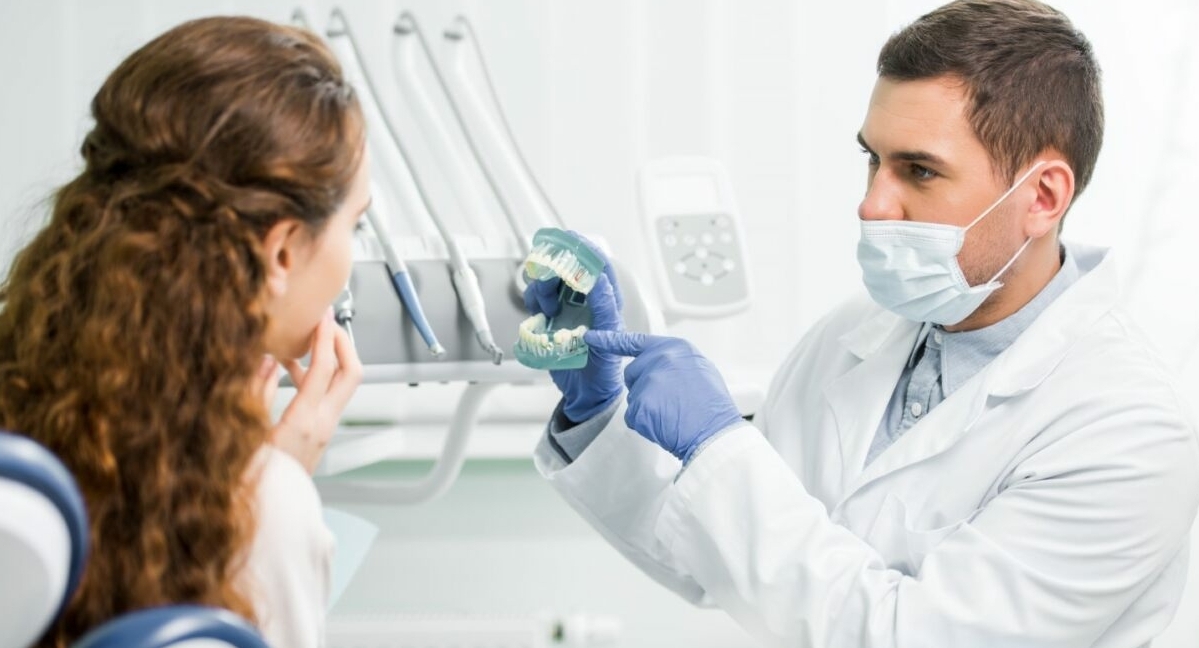 Un dentiste portant un masque médical tient des fausses dents pendant qu'il s'occupe d'un patient.