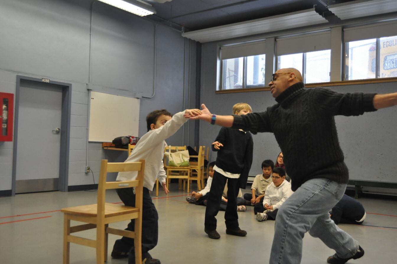 Un adulte encourageant un élève à danser dans une salle avec d'autres jeunes.