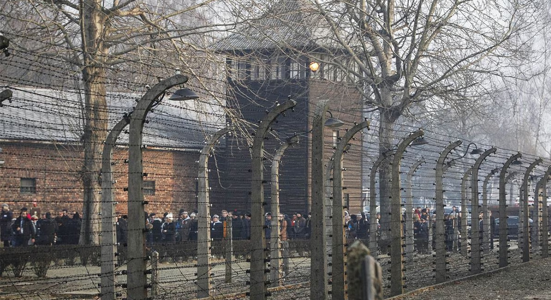 A large group of people lined up outside a building, behind a fence.