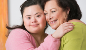 Photo of young adult woman with down syndrome hugging an elder female caregiver