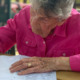 An older person sitting at a table, writing in a booklet.