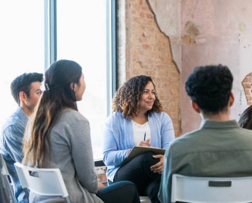 The diverse therapy group listens attentively as the young adult woman shares.
