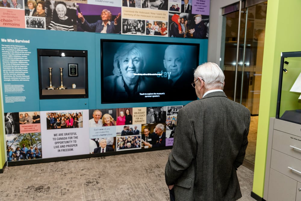 Older adult looking at museum exhibit with photos and video.