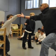 An adult encouraging a student to dance in a room of young people.