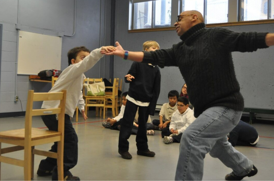 An adult encouraging a student to dance in a room of young people.