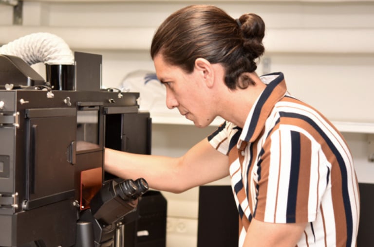 A person wearing a striped shirt adjusts a microscope.