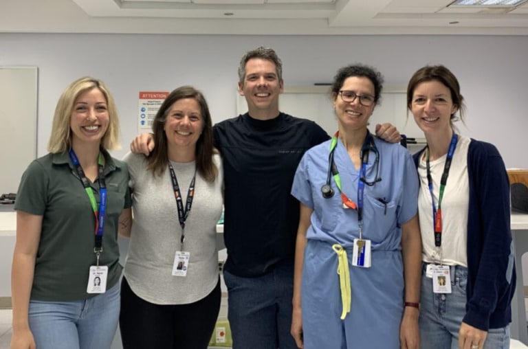 Five adults smiling for the photo. Most are wearing casual clothing, and one is wearing nurse scrubs.