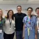 Five adults smiling for the photo. Most are wearing casual clothing, and one is wearing nurse scrubs.