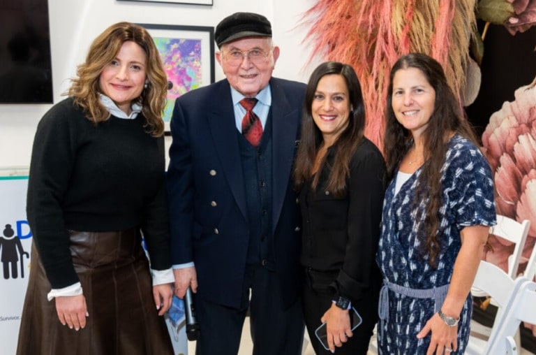 An older adult in a suit and tie poses for a photo with three other adults.