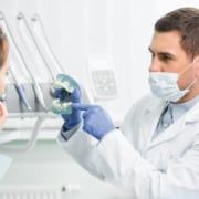 A dentist wearing a medical mask holds a set of false teeth while with a patient.
