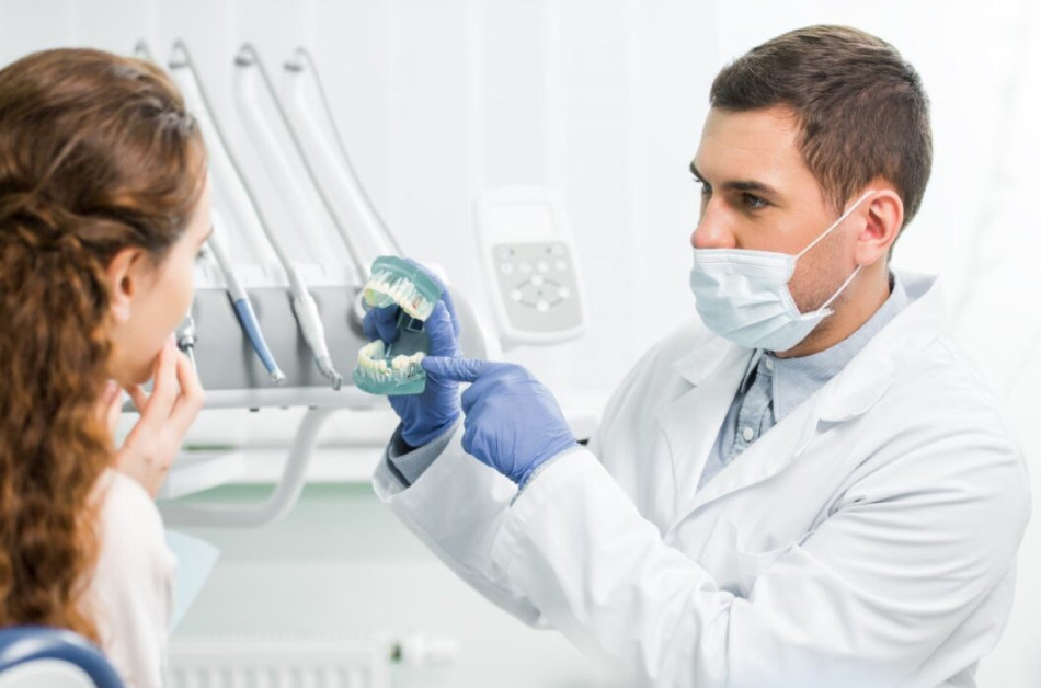 A dentist wearing a medical mask holds a set of false teeth while with a patient.