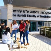A group of students and one service dog sit and talk in front of a building.