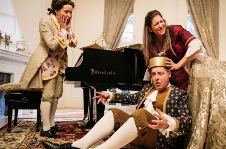 Three people in old English costumes. One sits confused on the floor, another tries to help them, a third looks on with concern.