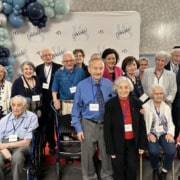 A large group of adults of varying age smile for a photo. They stand in front of a backdrop that reads "Celebrate 18".