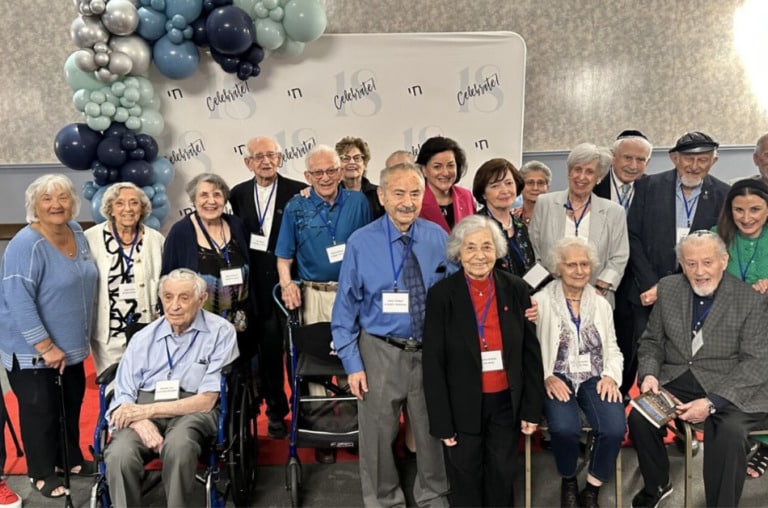A large group of adults of varying age smile for a photo. They stand in front of a backdrop that reads "Celebrate 18".