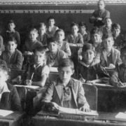 A black and white photo of young students at their desks in a crowded classroom.