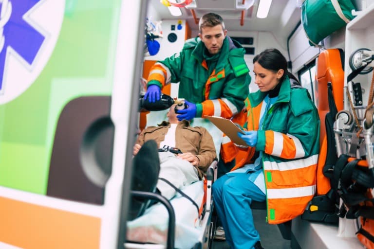 Two emergency response workers in the back of an ambulance with a patient.